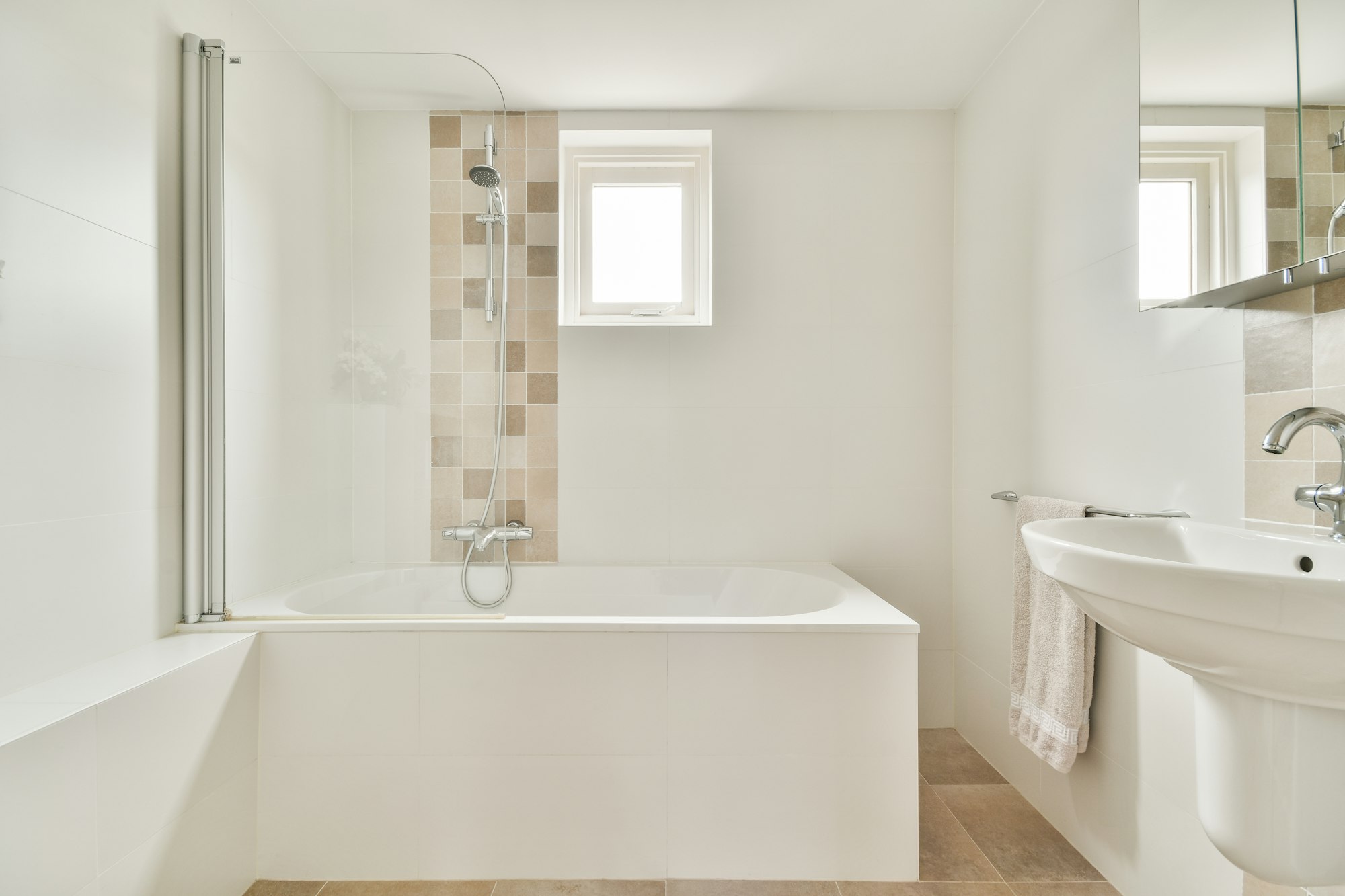 Modern white bathroom with bathtub, shower, sink, and window. No grab bars visible, potential slip hazards present.